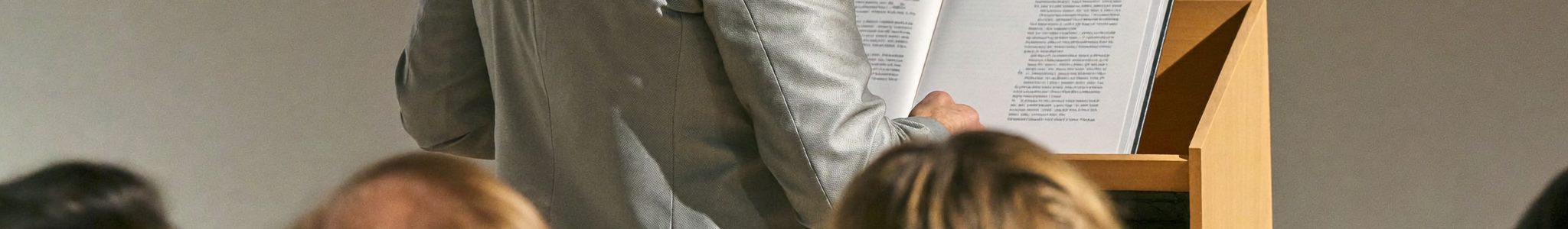 Dozent unterrichtet am Pult vor einer Lerngruppe